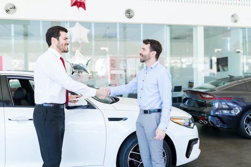 Improve Car Sales, customer shaking hands with car salesman at dealership.