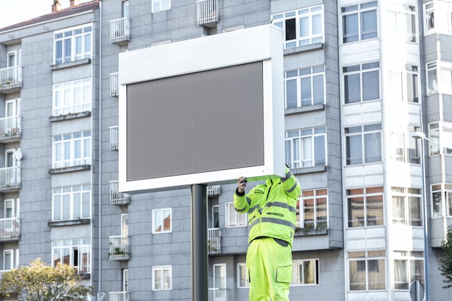 Construction Site Advertising, person installing an electronic sign near a building.
