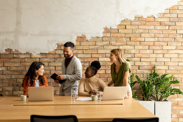 Renovate Office, a group of people working at the office desk in front of a brick wall design.