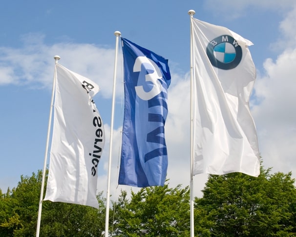 Benefits of advertising flags, 3 branded flags on tall white flagpoles.