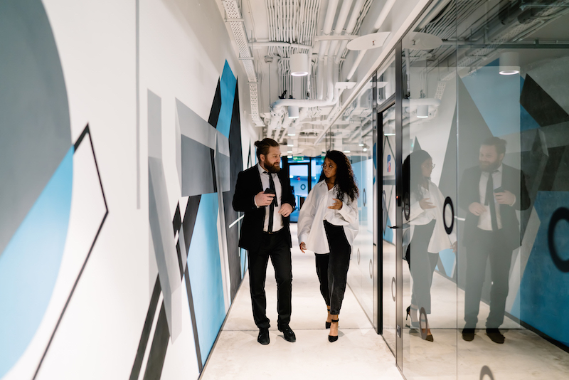 Office branding, man and woman walking through office halls near creative wallpaper